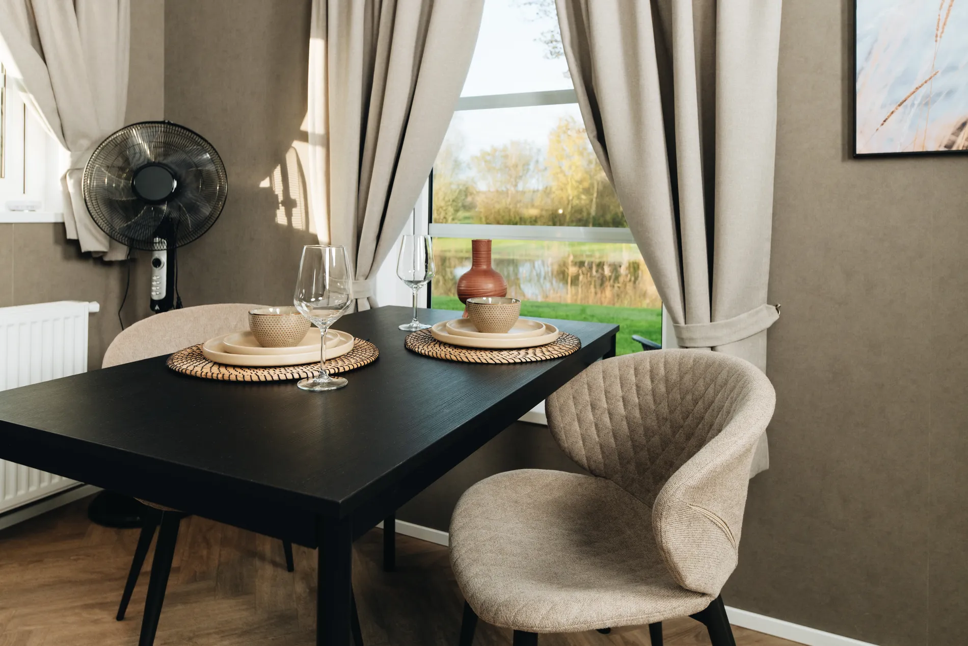 Sfeervol gedekte zwarte eettafel voor twee personen in een vakantiewoning, voorzien van modern servies, wijnglazen en een rustgevend uitzicht op het water.